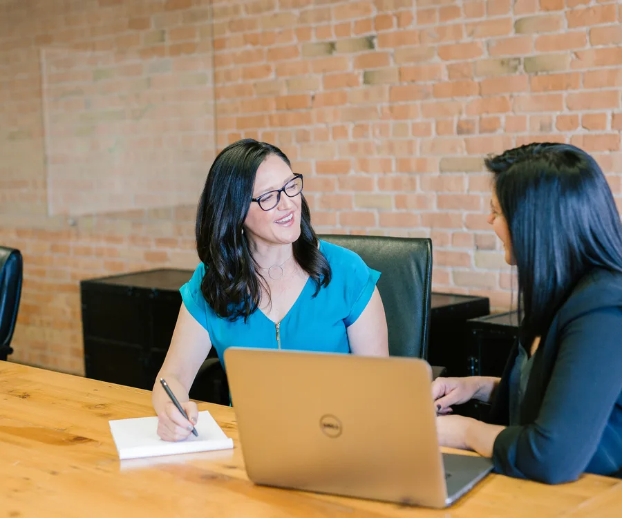 Two accounting professionals reviewing notes together at a table during a client meeting.
